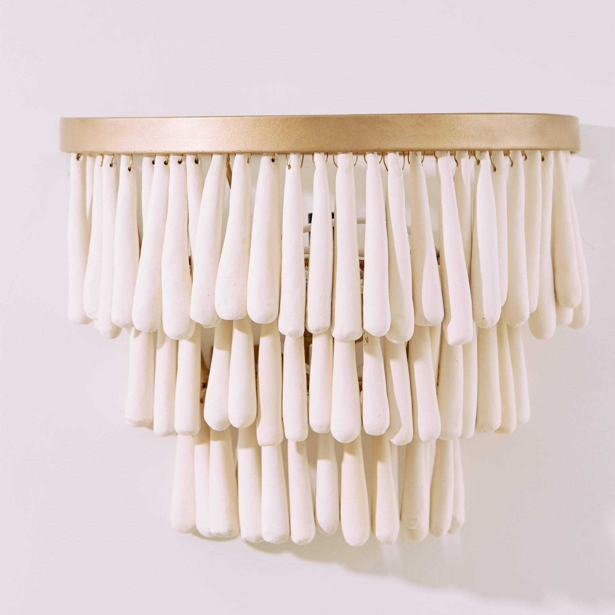 Decorative wall light fixture with white beads and gold base on a white background